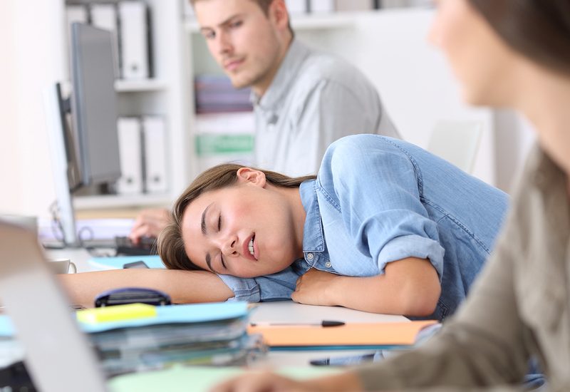 A young woman suffering the effects of sleep deprivation by falling asleep at her desk.