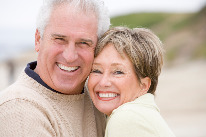 A mature woman and man smiling on a beach.
